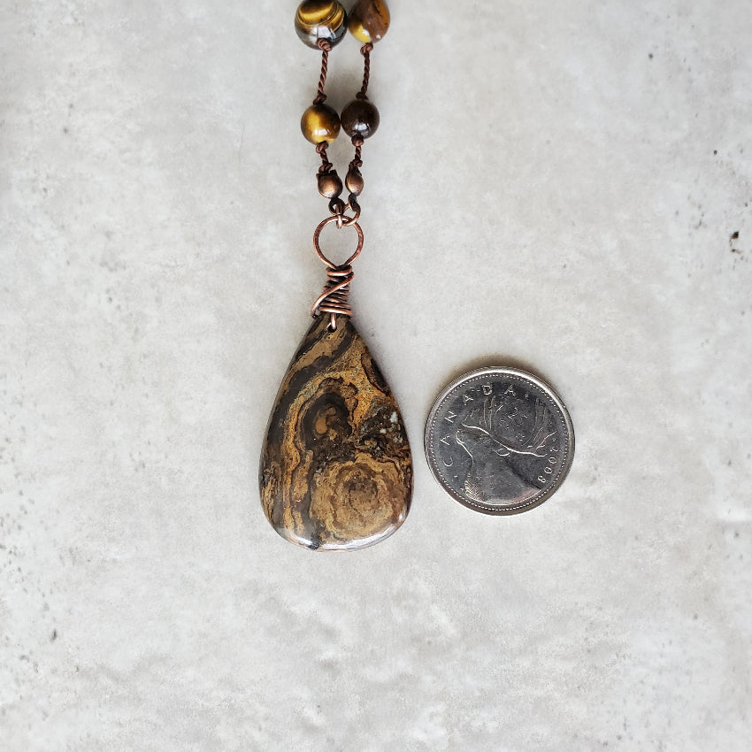 Teardrop-shaped pendant with marbled pattern next to a coin on a textured surface
