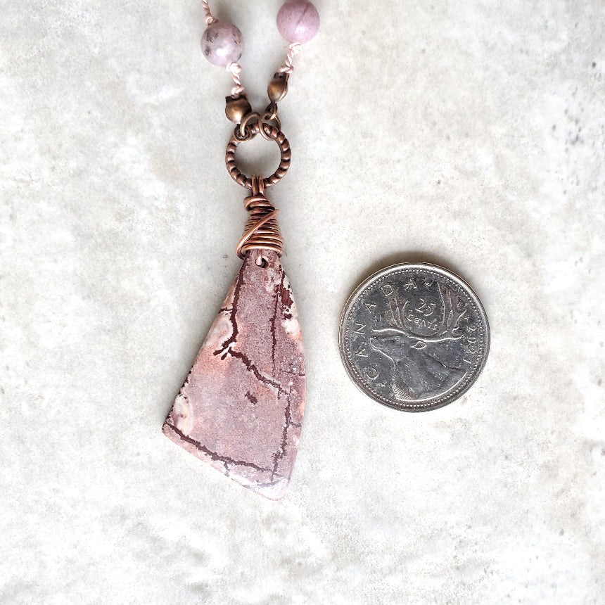 Necklace with a pink stone pendant next to a coin on a white background