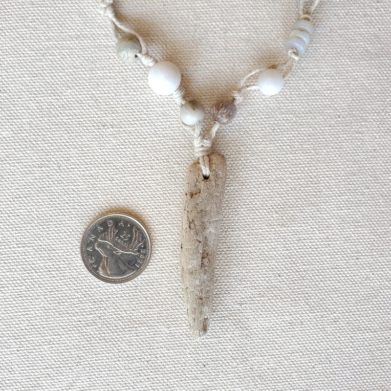 Necklace with a large driftwood pendant next to a coin for scale on a textured fabric background