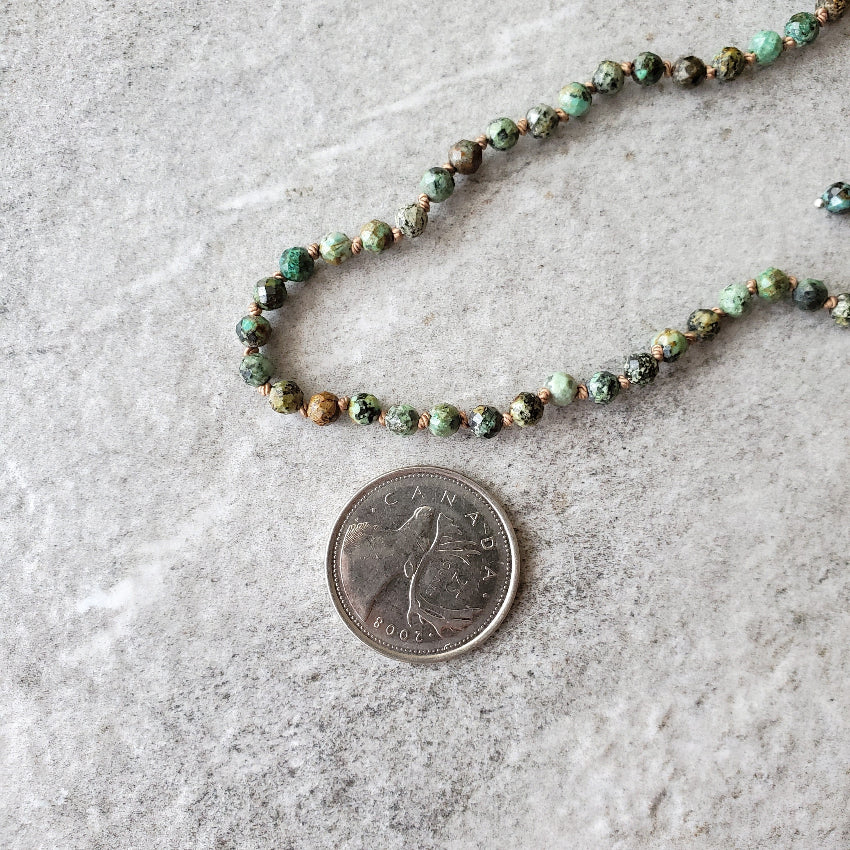 Faceted African Turquoise hand knotted necklace beside a quarter