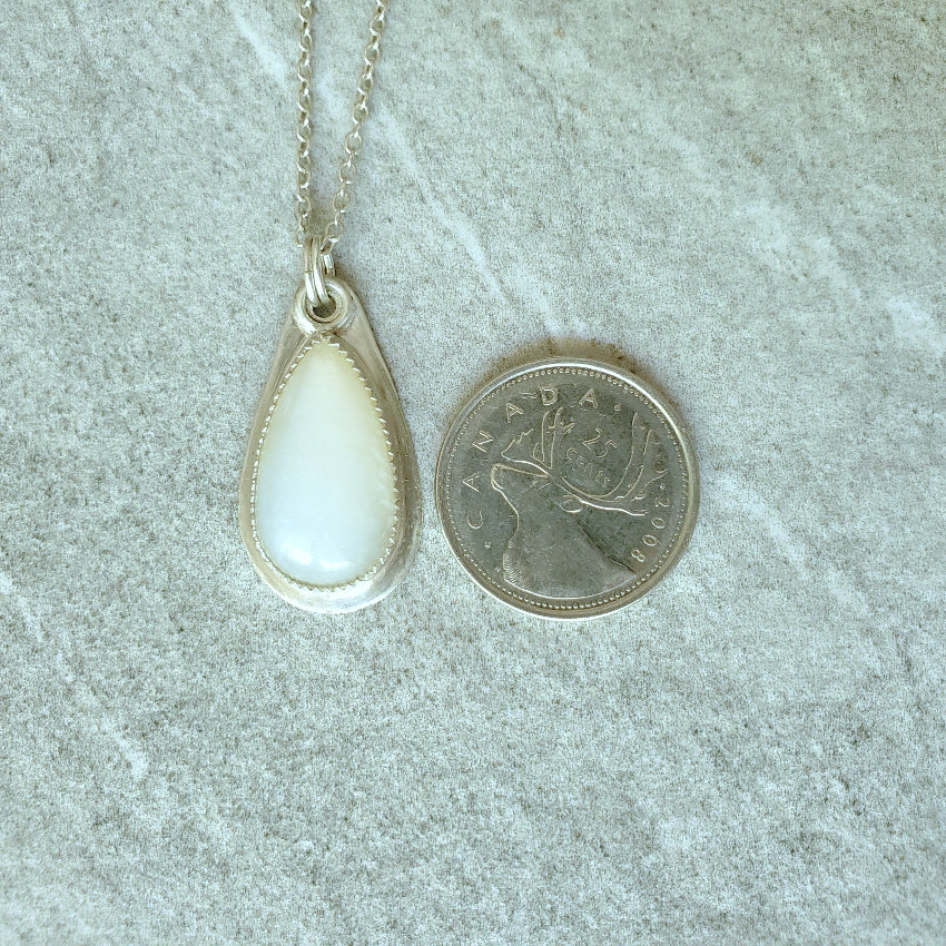 Teardrop-shaped Moonstone silversmith pendant on a chain next to a Canadian quarter on a textured surface