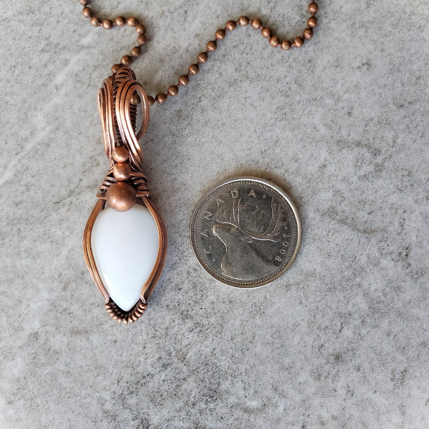 White Opal copper wire wrap pendant beside a quarter