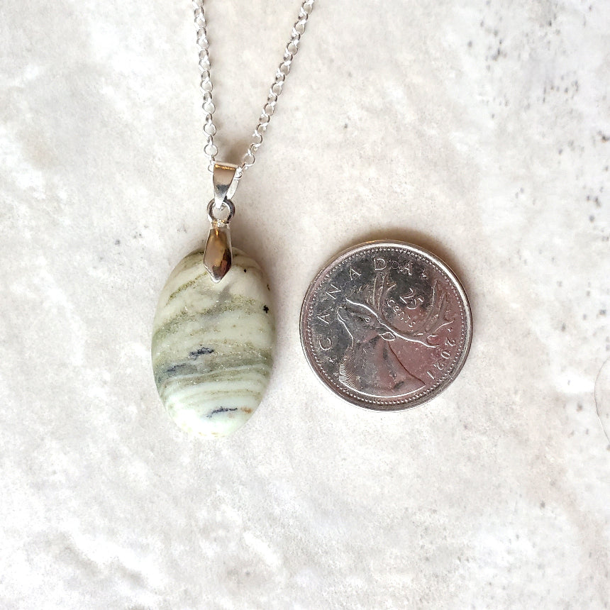 Serpentine oval pendant necklace beside a quarter