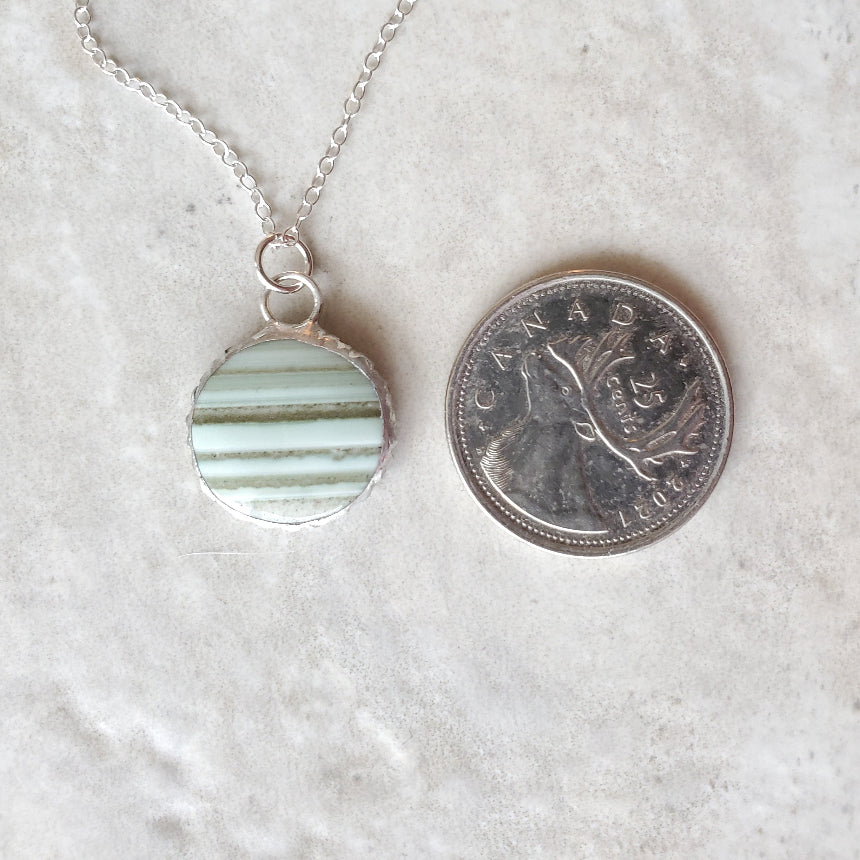 Green Saturn Chalcedony Round pendant necklace beside a quarter