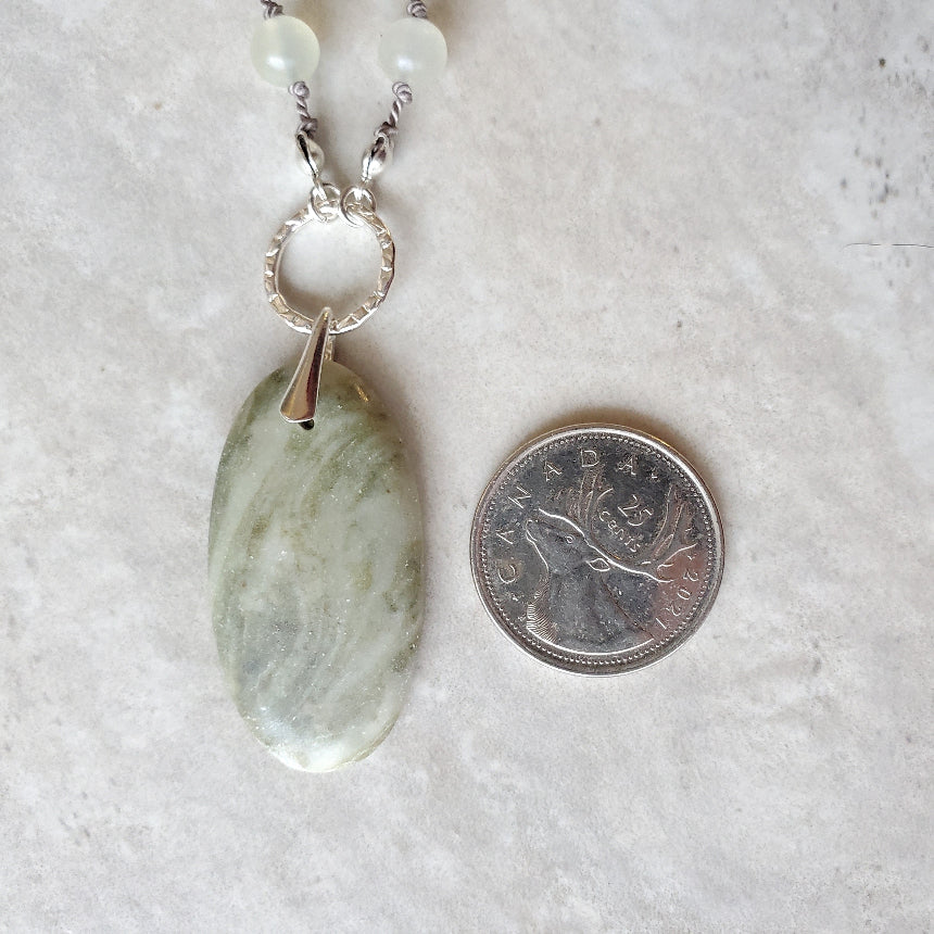 Beaded gemstone necklace with Serpentine focal beside a quarter