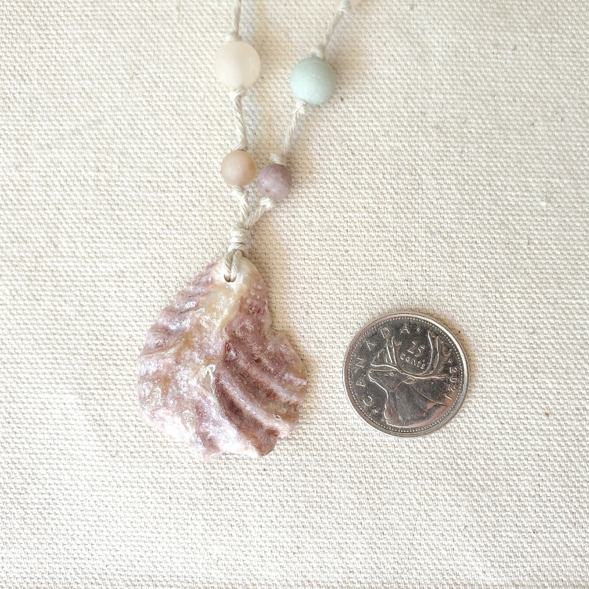 Necklace with a shell pendant next to a coin on a textured surface