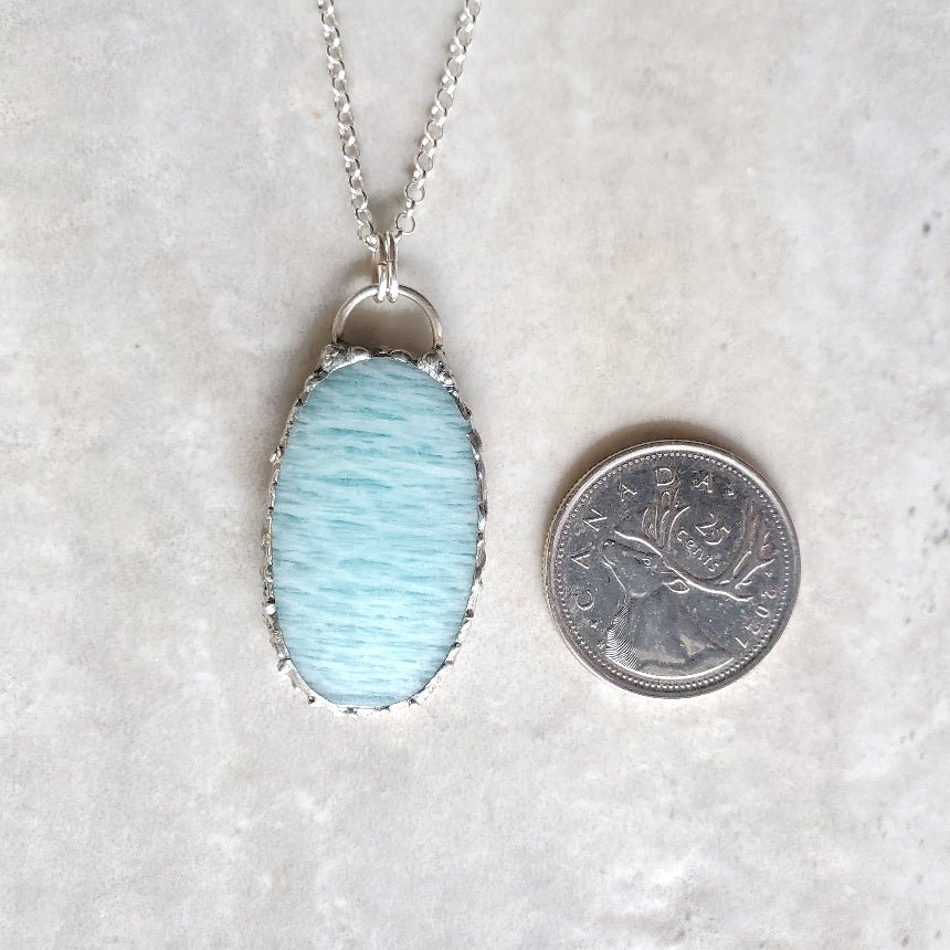 Amazonite oval pendant beside a quarter