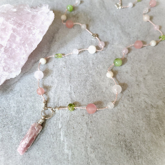 Beaded necklace with a pink Tourmaline focal pendant on a textured surface