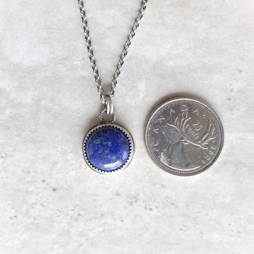 Lapis Lazuli silversmith pendant necklace beside a quarter