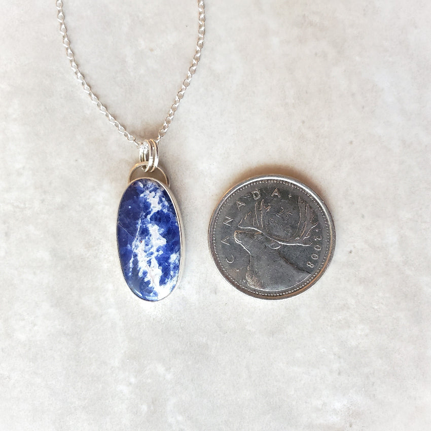Sodalite silversmith pendant beside a quarter
