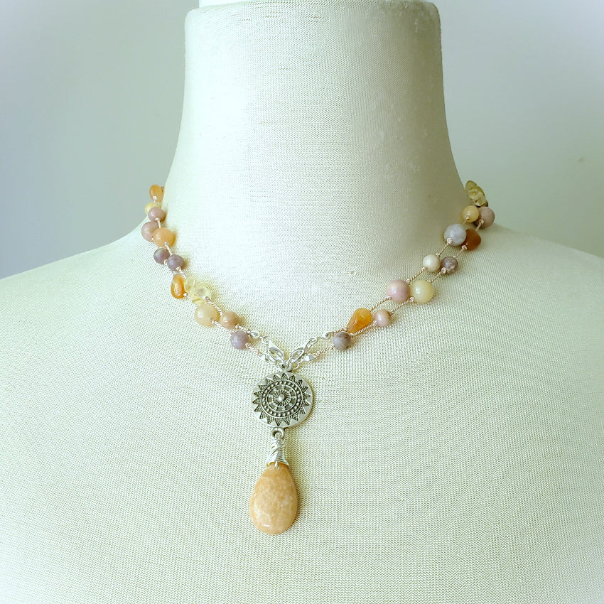 Necklace with multi coloured gemstone beads and a pendant on a mannequin bust against a white background