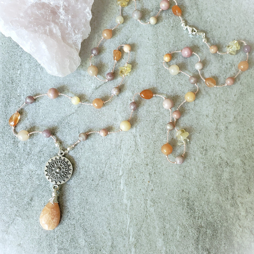 Necklace with peach-colored beads and a silver pendant on a textured surface