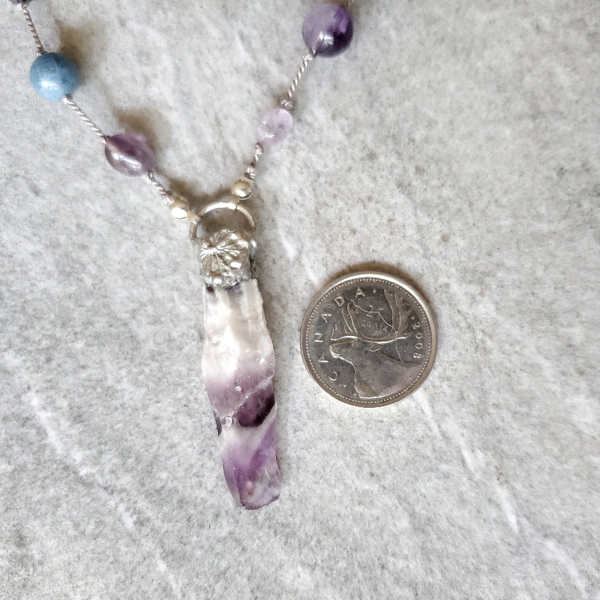 Necklace with an Amethyst pendant next to a quarter on a gray surface