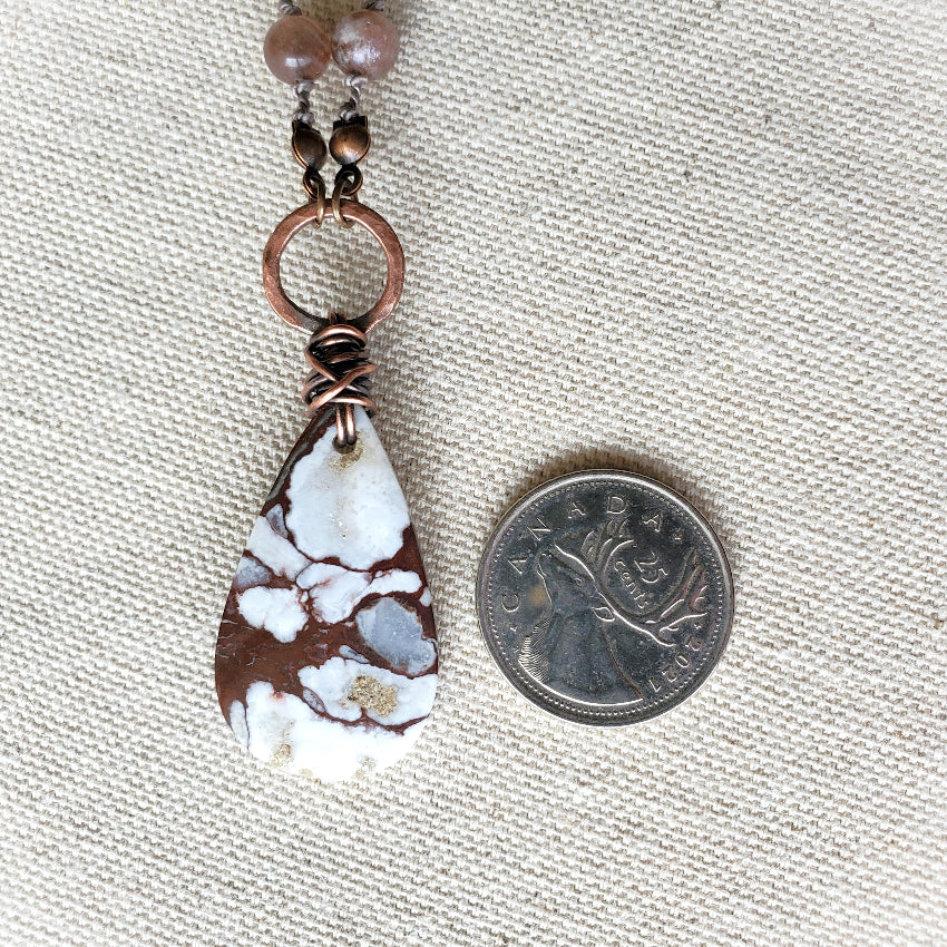 Stone teardrop pendant with copper wire wrapping on a fabric background
