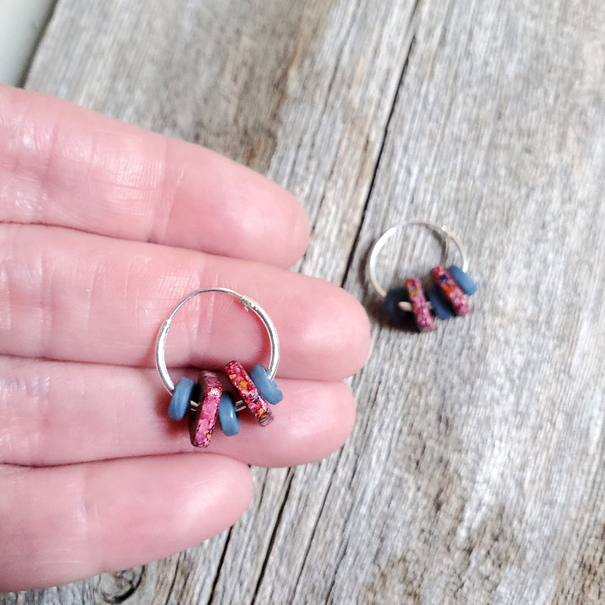 Silver hoop earrings with colorful beads held in a hand on a wooden surface