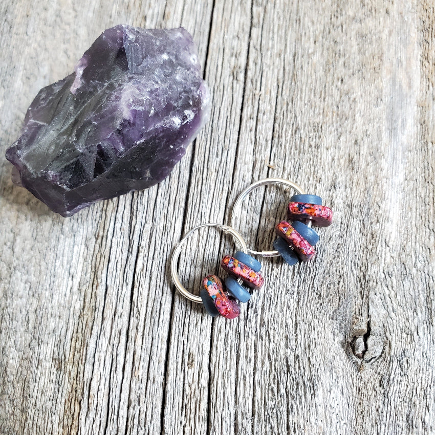 Pair of hoop earrings with colorful beads on a wooden surface next to an amethyst crystal.