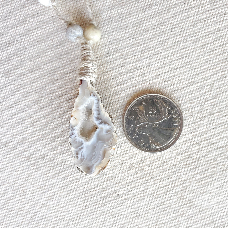 Jewelry with a large stone and beads next to a quarter for scale on a textured beige background