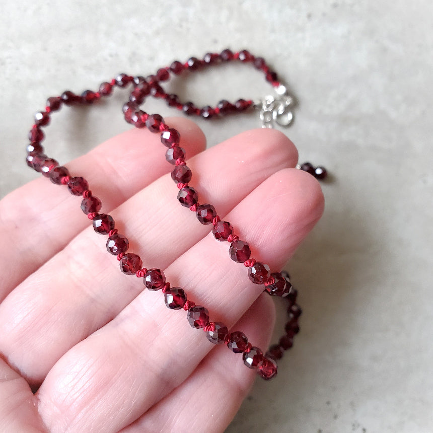Faceted Garnet necklace held in a hand against a neutral background