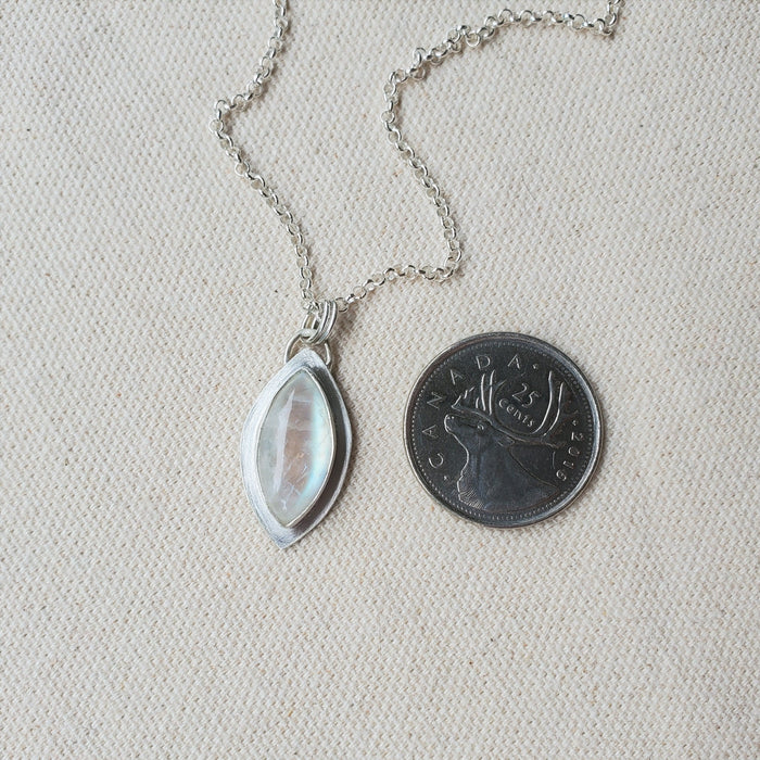 Rainbow moonstone marquise bezel set pendant beside a quarter