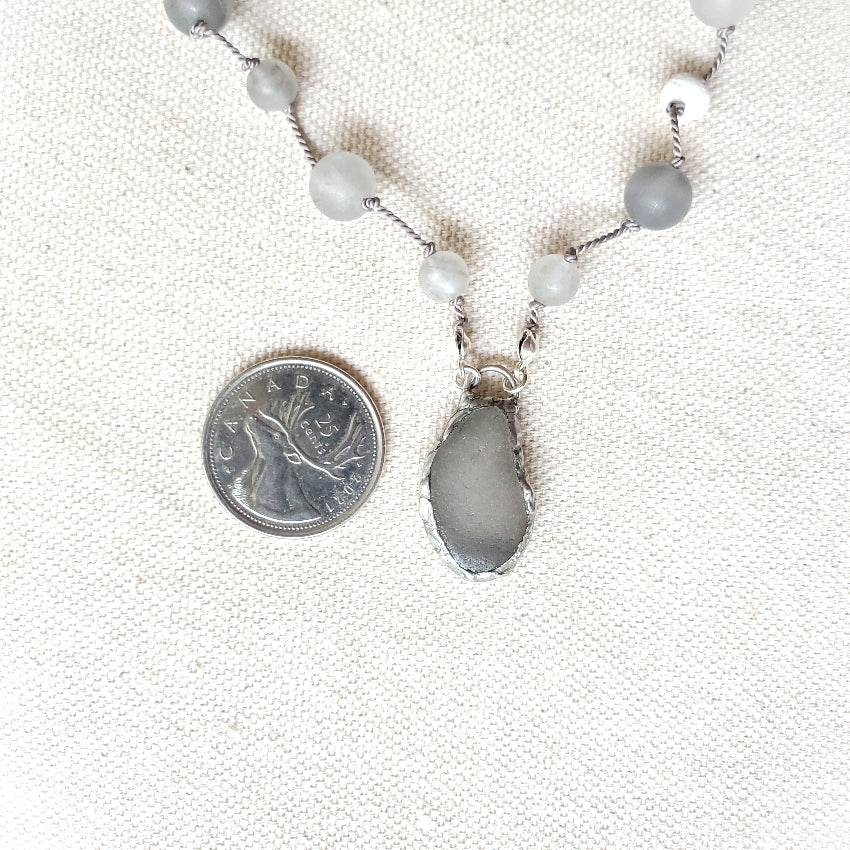 Necklace with gray pendant and beads next to a quarter on a textured white background