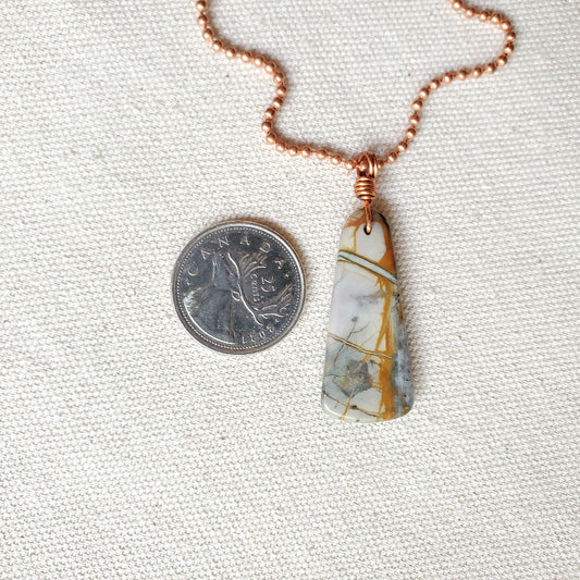 Necklace with a pendant next to a quarter on a textured white background