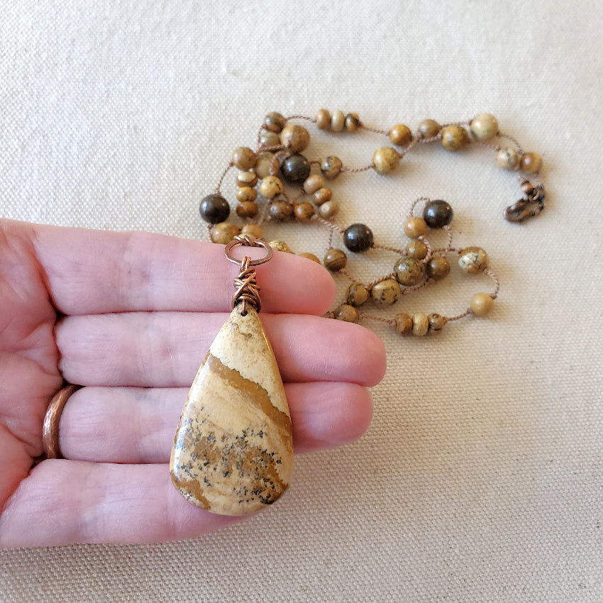 Beaded necklace with a teardrop pendant held by a hand on a beige fabric background