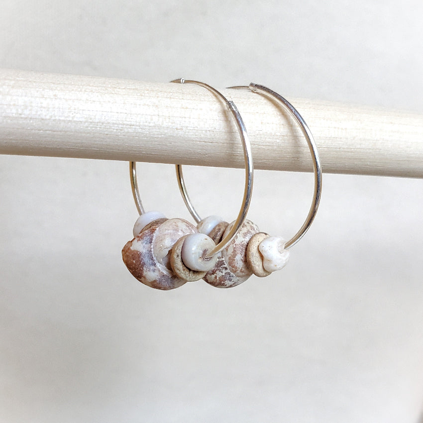 Silver hoop earrings with shell-like beads on a white background