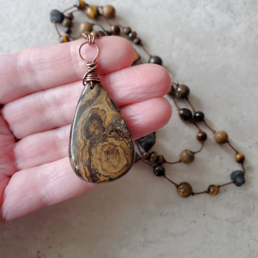 Hand holding a necklace with a teardrop-shaped pendant against a neutral background