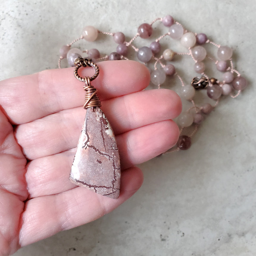 Necklace with a pink stone pendant held in a hand on a light background