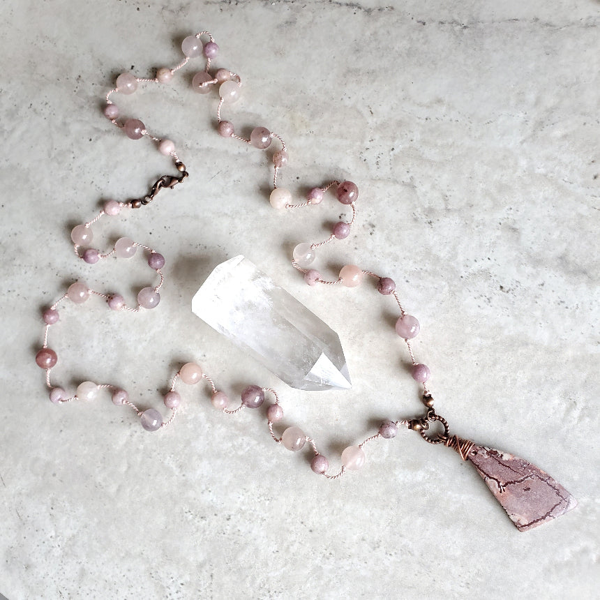 Necklace with pink beads and a pendant on a light gray surface