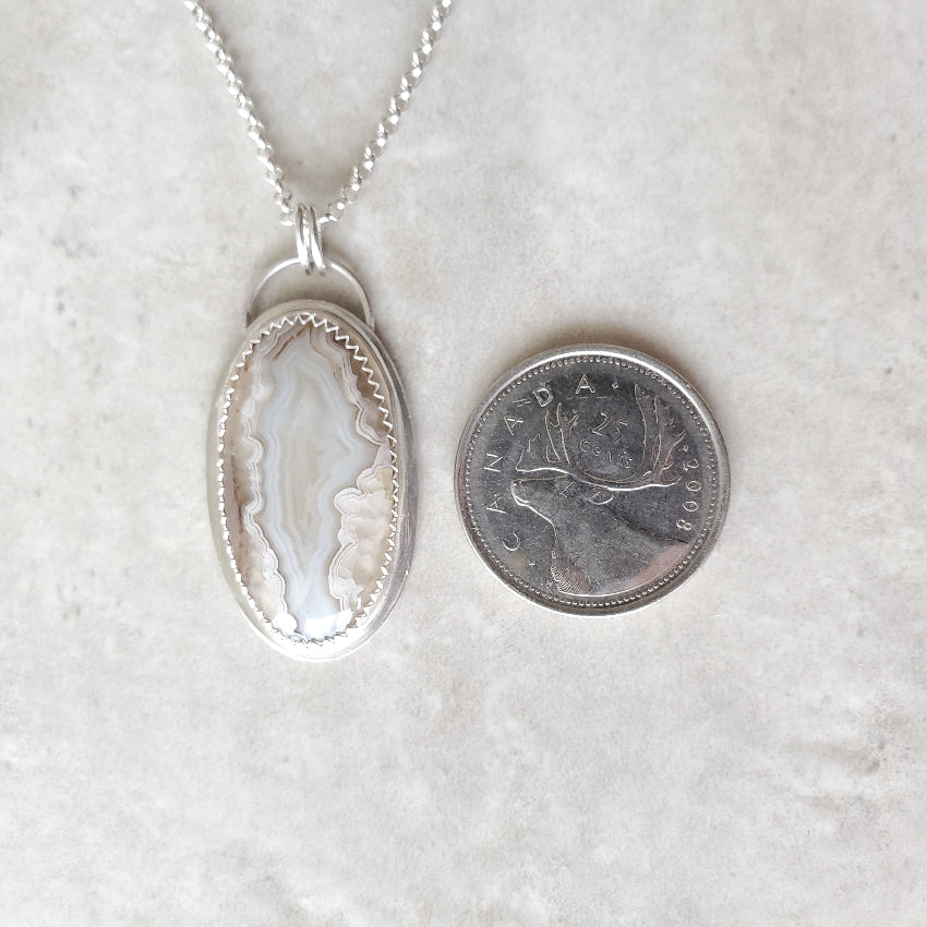 Crazy Lace Agate silversmith pendant beside a quarter
