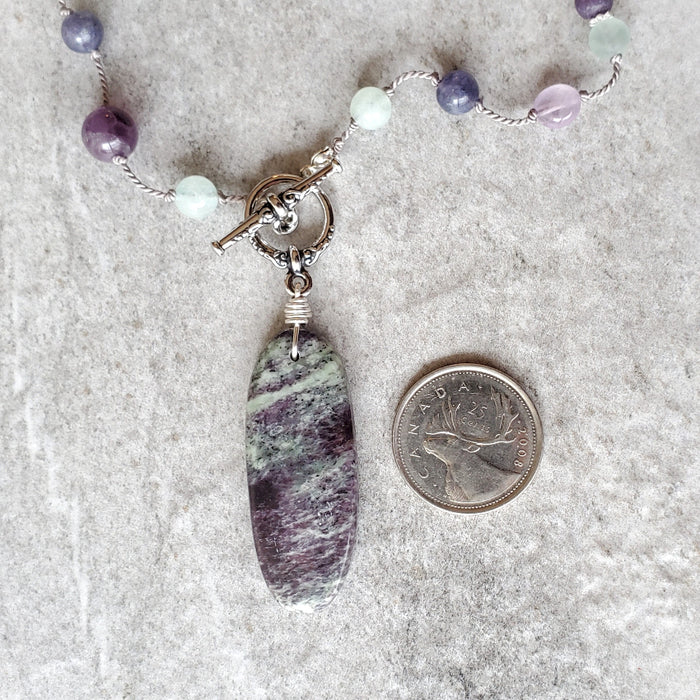 Purple and Green gemstone knotted necklace beside a quarter