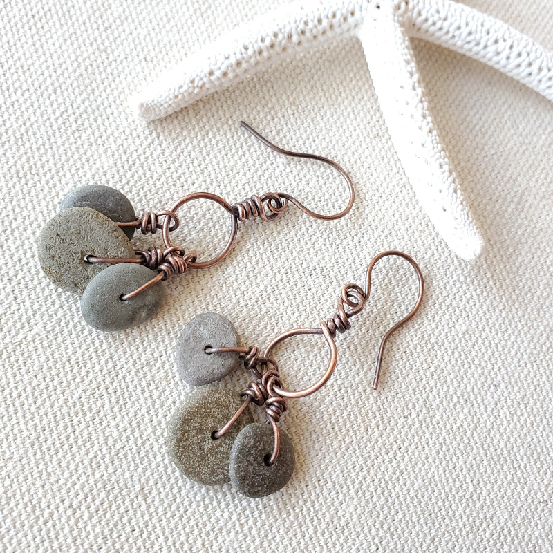 Pair of earrings with gray stones and copper wire on a textured white surface