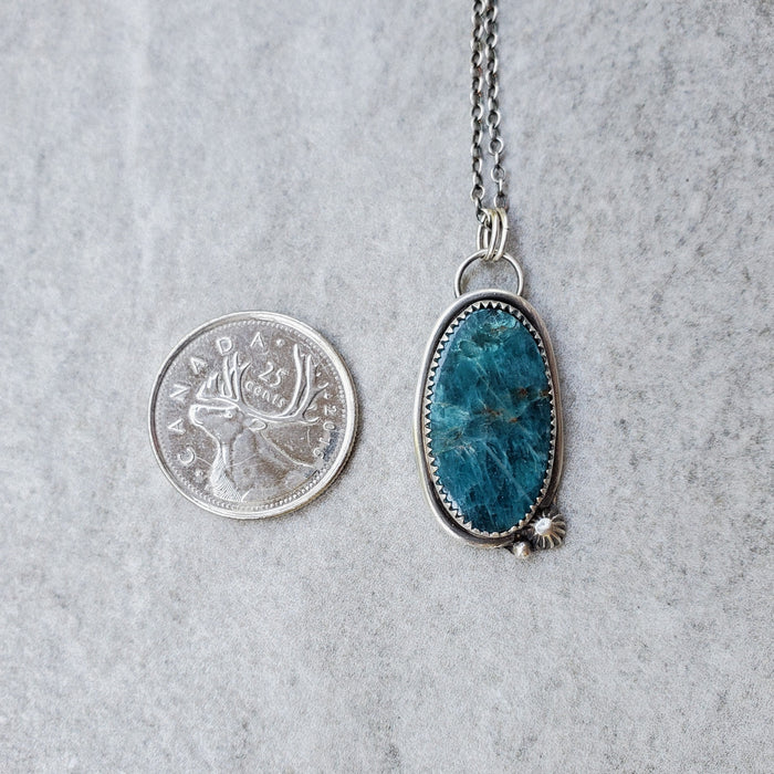 Blue Apatite oval silversmith pendant beside a quarter