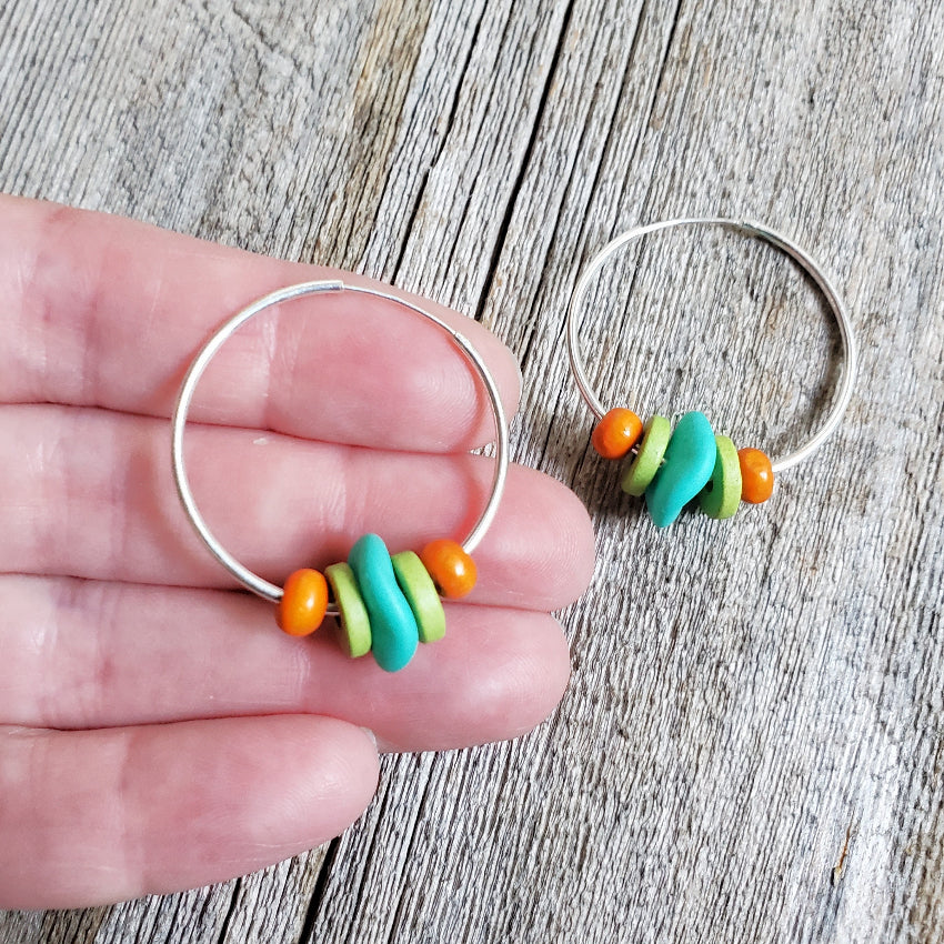 Hoop earrings with colorful beads held by a hand on a wooden surface