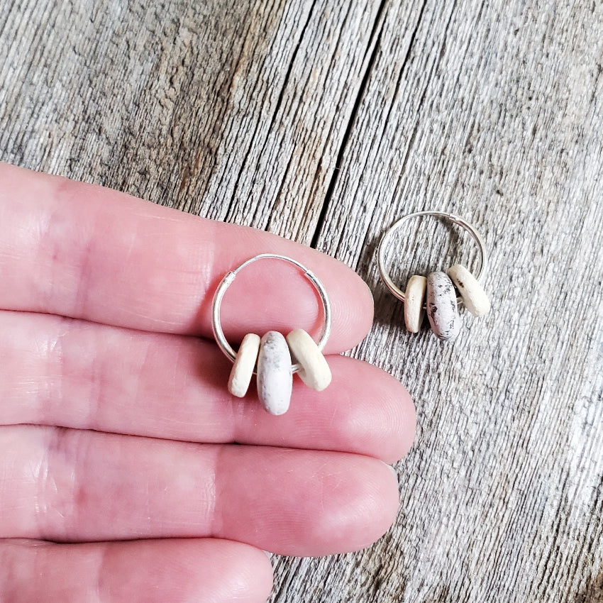 Silver hoop earrings with beige beads on a hand and wooden surface
