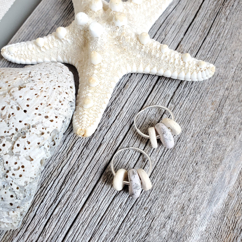 Pair of earrings with white and silver beads on a wooden surface with a starfish and shell.