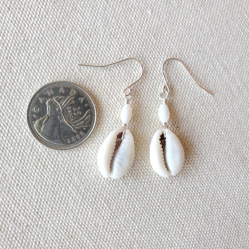 Cowrie shell dangle earrings beside a quarter