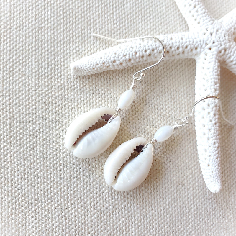 Shell earrings on a textured beige surface with a starfish.