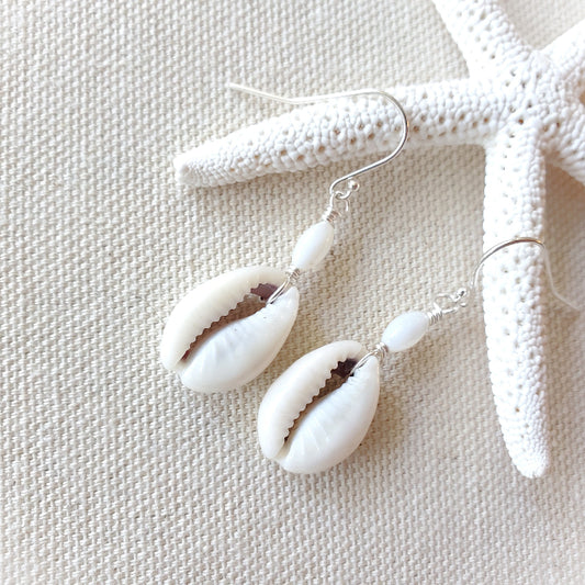 Shell earrings on a textured beige surface with a starfish.