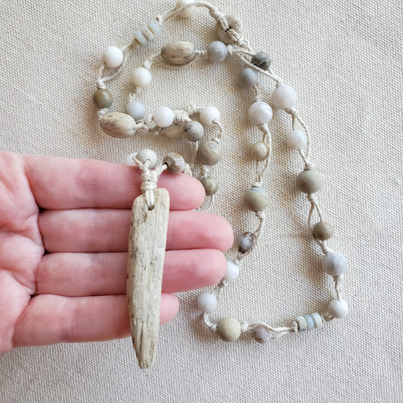 Necklace with natural elements held in a hand on a beige background