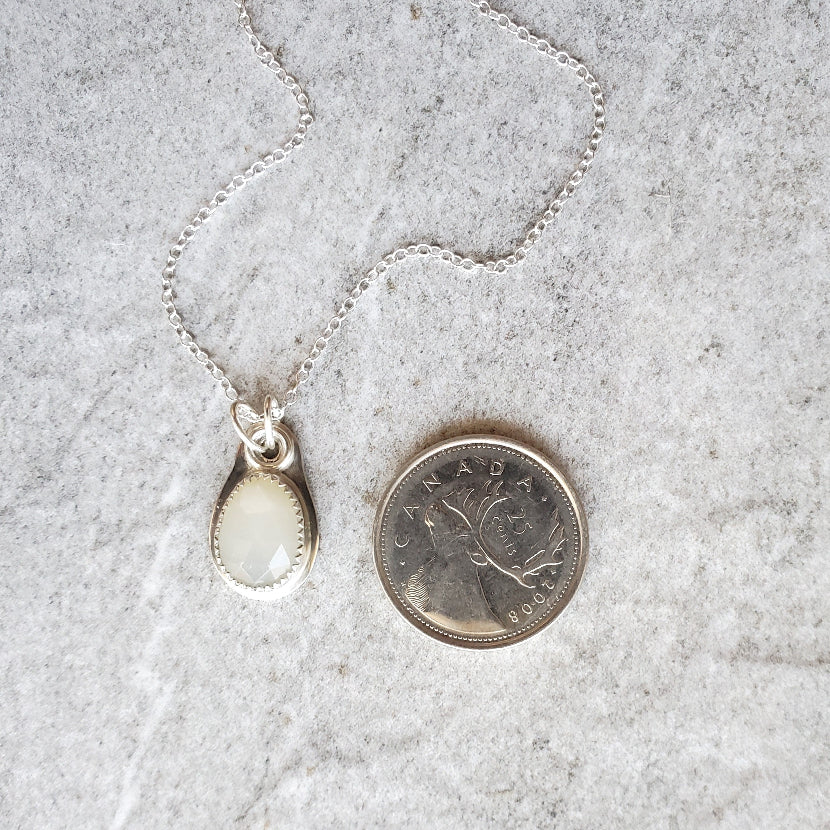 faceted white moonstone sterling silver pendant beside a quarter
