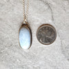 Blue Opal oval pendant set in silver beside a quarter