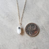 White Moonstone point sterling silver necklace beside a quarter