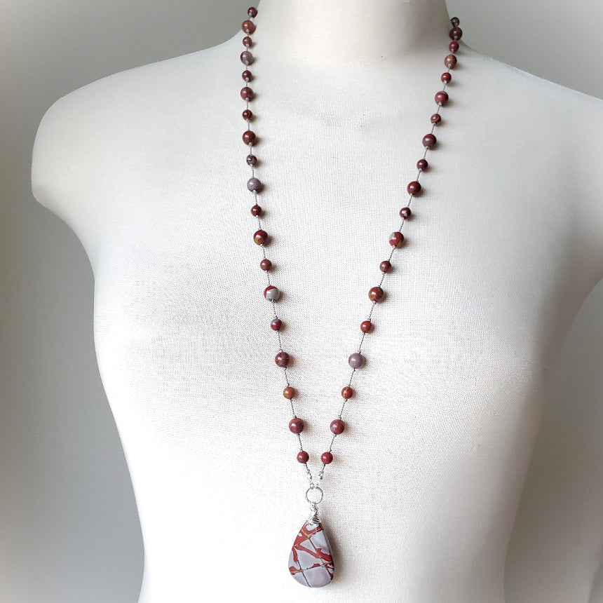 Necklace with red beads and a large stone pendant on a mannequin against a gray background