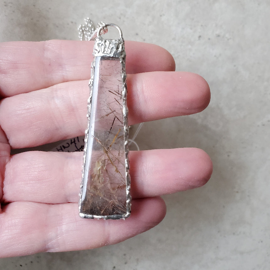 Silver pendant with natural elements held in a hand against a neutral background
