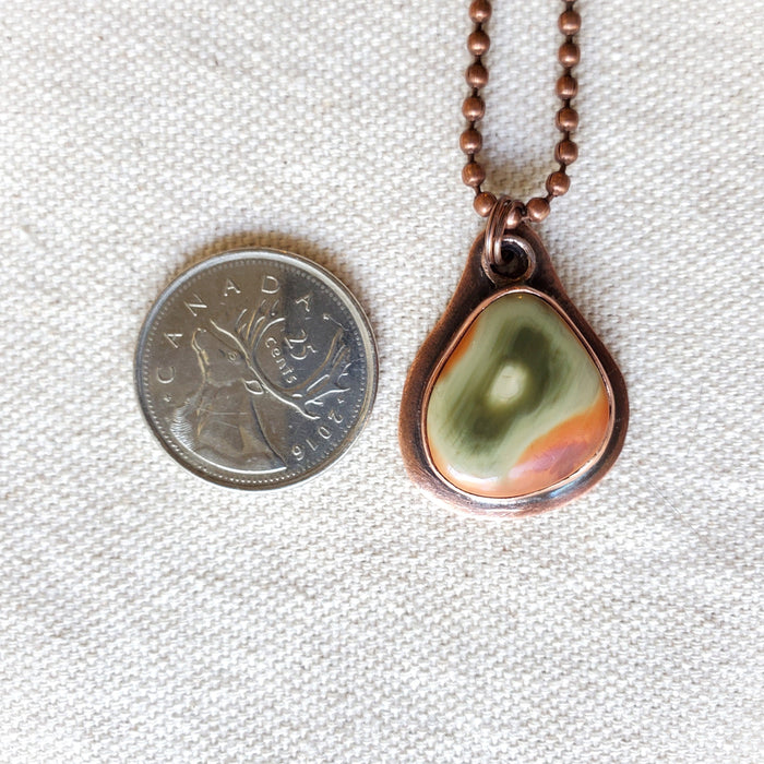 Freeform Imperial Jasper copper metalsmith pendant beside a quarter