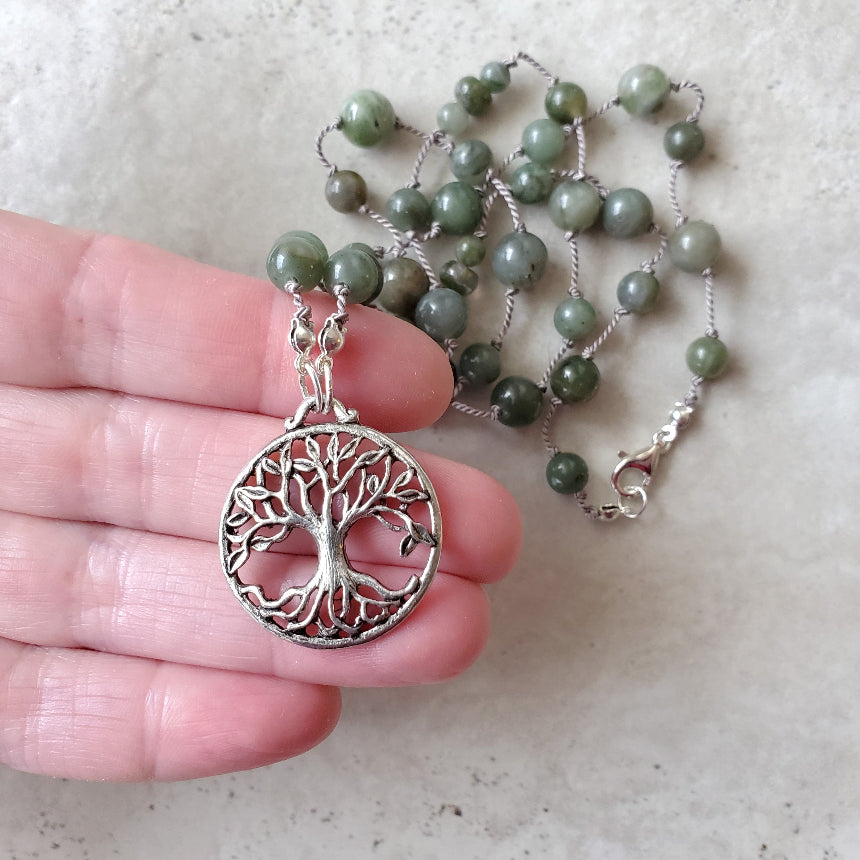 Necklace with African Jade beads and a silver tree of life pendant held by a hand on a light background