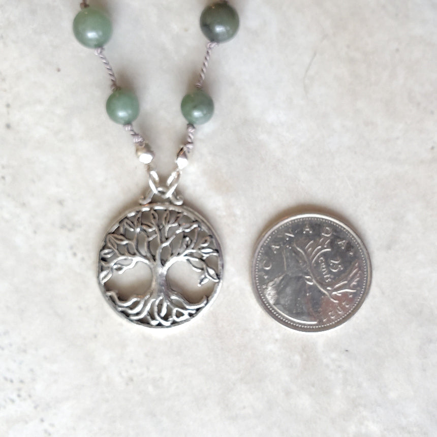Necklace with tree of life pendant next to a quarter on a white background
