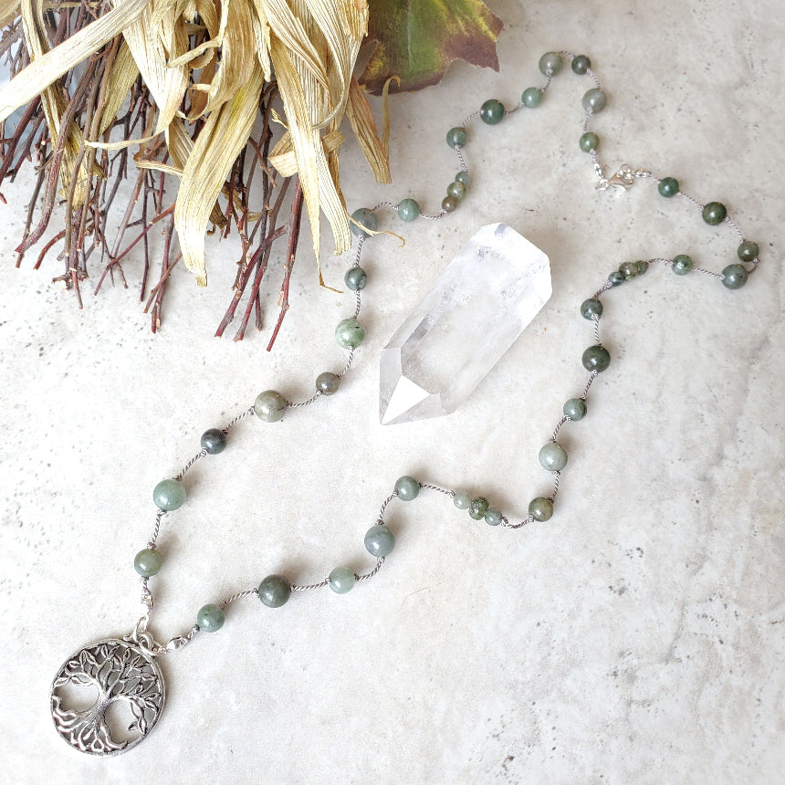 Necklace with African Jade beads and a tree of life pendant on a textured surface with a crystal and branches.